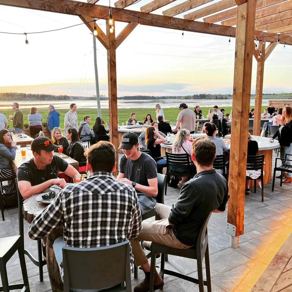 Guests under the wooden pergola at the Lone Oak Beer Garden with a view of the water