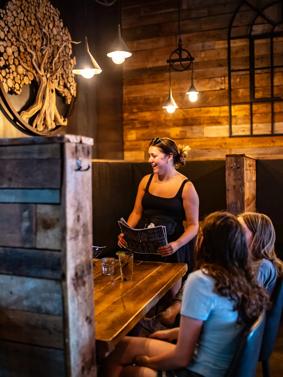 Server chatting with guests in a reclaimed-wood booth at the Lone Oak Brewpub
